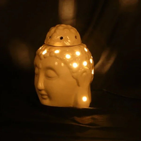 Ceramic Buddha head aroma oil burner with glowing light holes on dark background