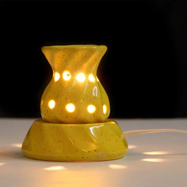 Yellow ceramic electric aroma oil burner with cut-out holes, lit on a white surface.