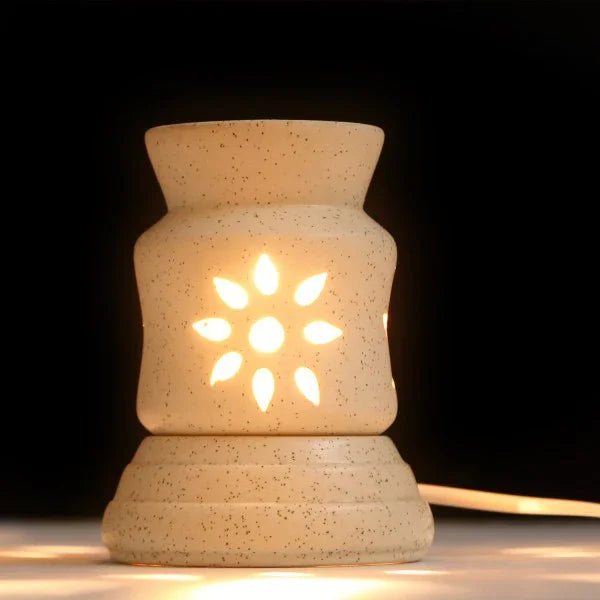 Electric ceramic aroma oil burner with glowing flower cutout design on a dark background