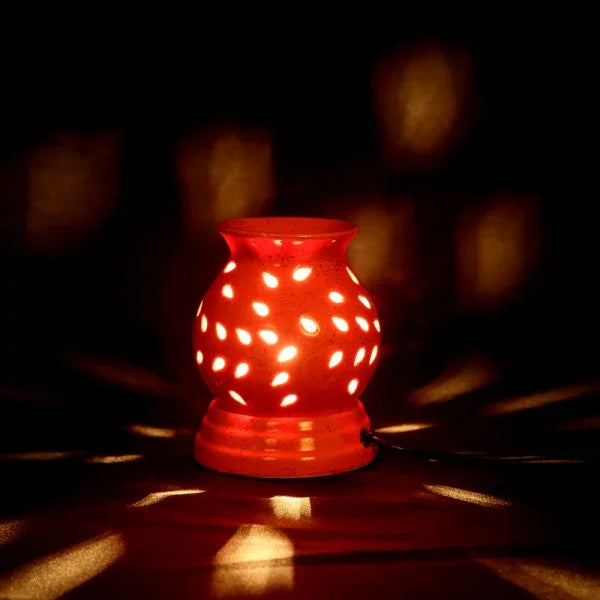 Ceramic electric aroma oil burner with glowing perforated design, lit in a dark setting